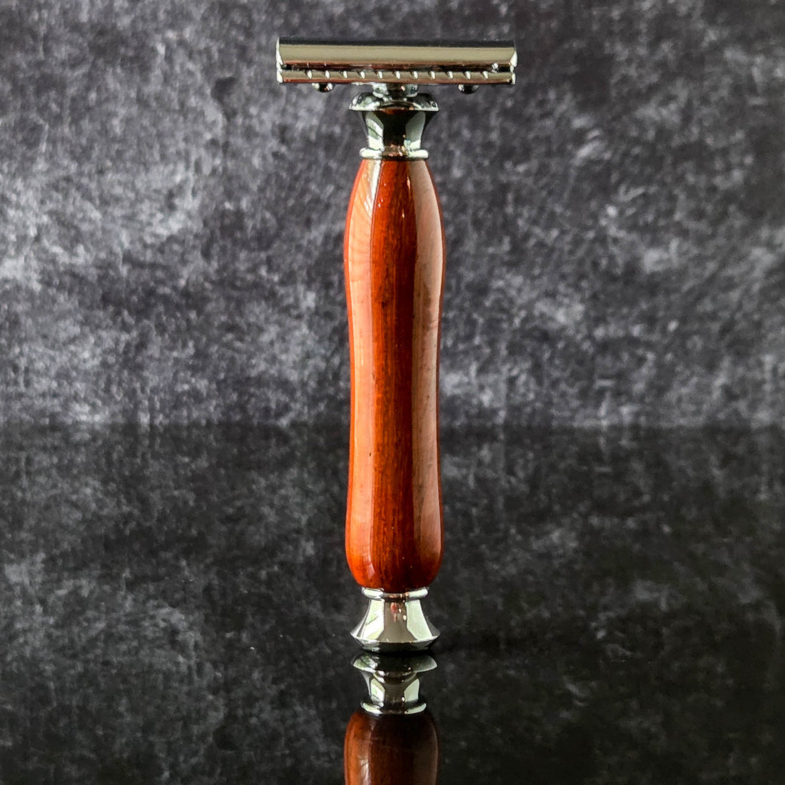 Shaving razor with a red wooden handle  made from padauk on a dark surface