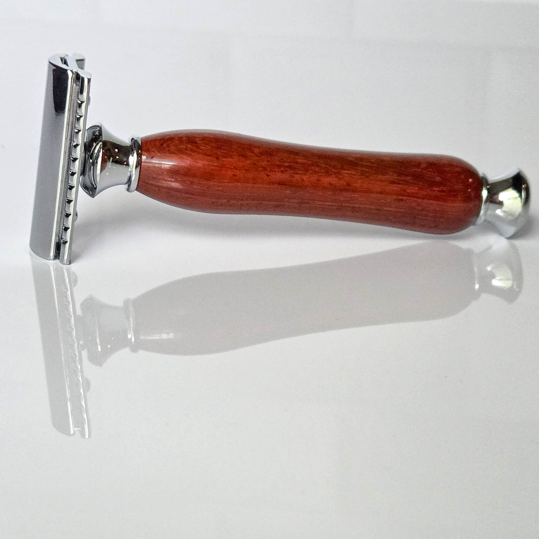 Shaving razor with a traditional wooden handle made from padauk on a white reflective background