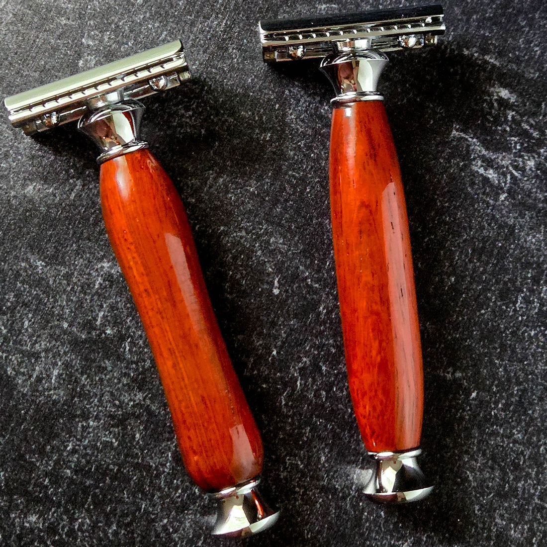Two razors with traditional and modern handles made from padauk on a dark textured surface