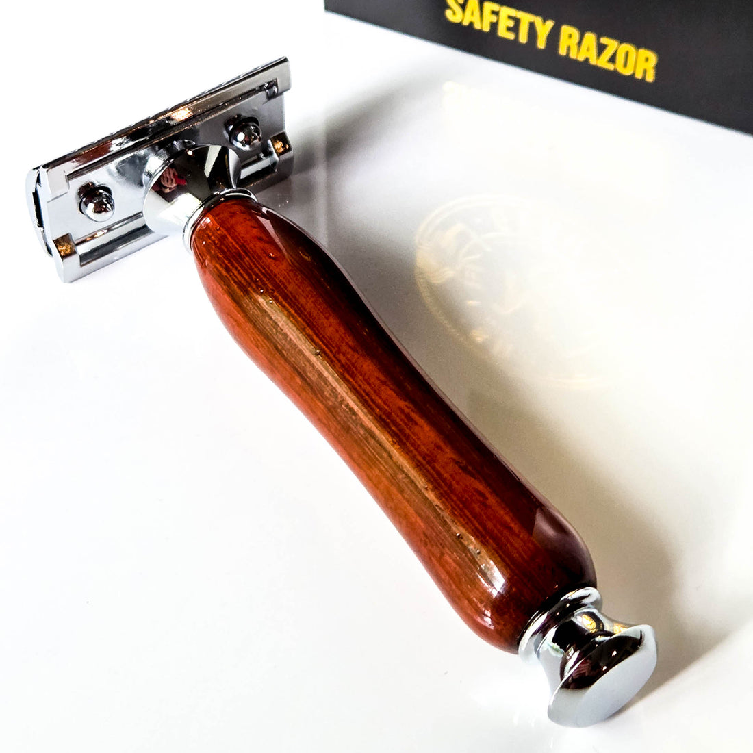 Safety razor with traditional wooden handle made from padauk on a white background with a gift box in the background